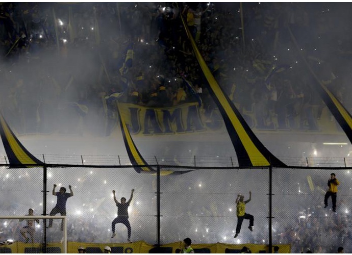 Packed terrace at night, fans waving flags and flares