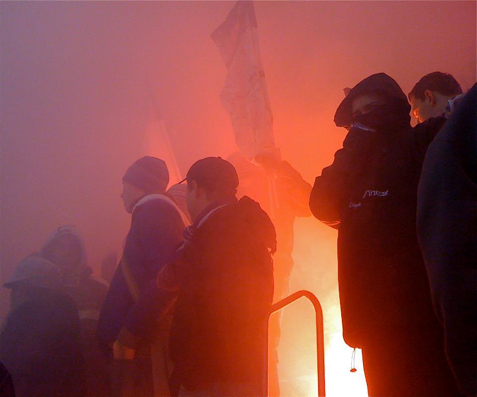 Ultras behind a banner in a haze of red flare smoke